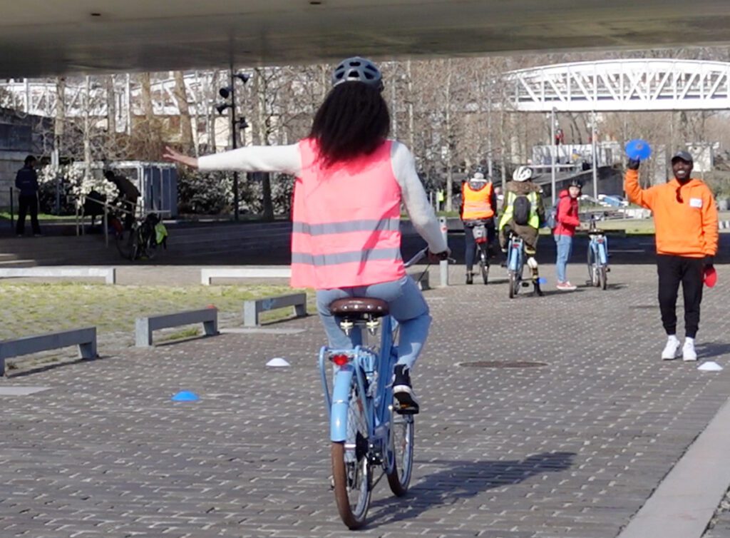 Une apprenante à vélo indique la gauche avec son bras