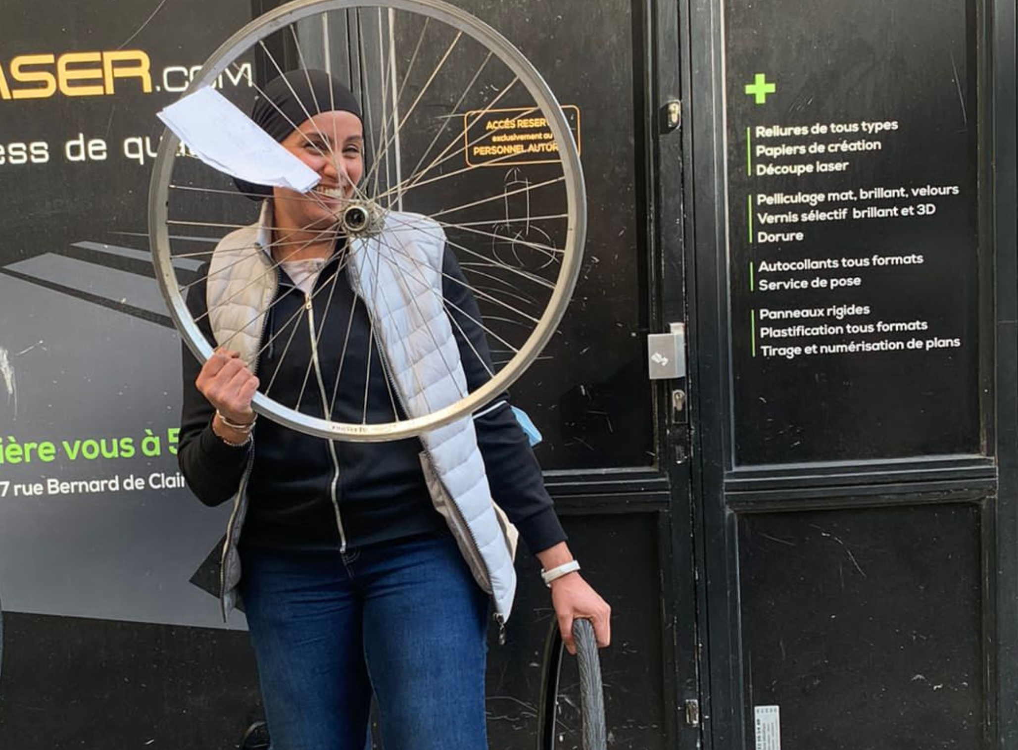 Une femme souriante porte une roue de vélo devant son visage